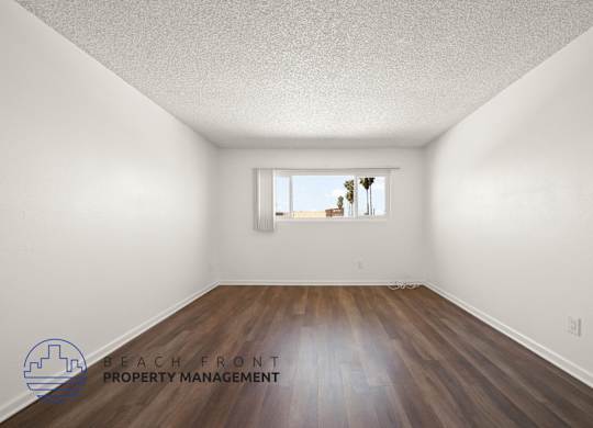 A room with wooden floors and a window showing a view of palm trees.