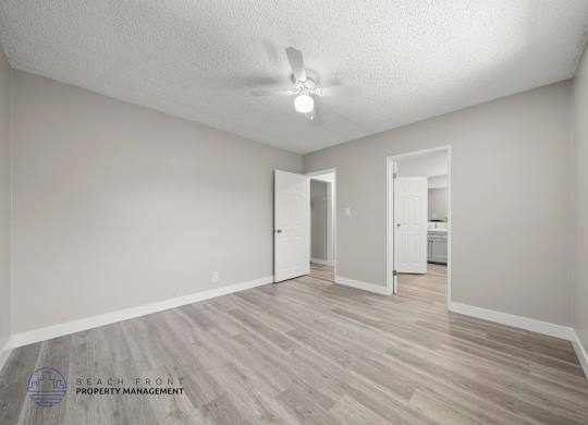 A spacious room with a ceiling fan and light, and a wooden floor.