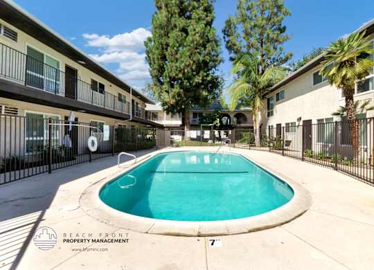 A pool surrounded by a black fence and a building with balconies.
