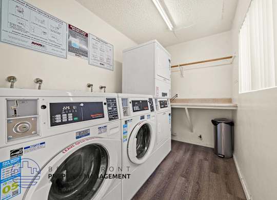 A laundry room with washers and dryers and a trash can.