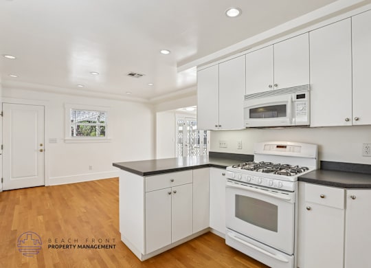 A kitchen with white cabinets and appliances, and a wooden floor.