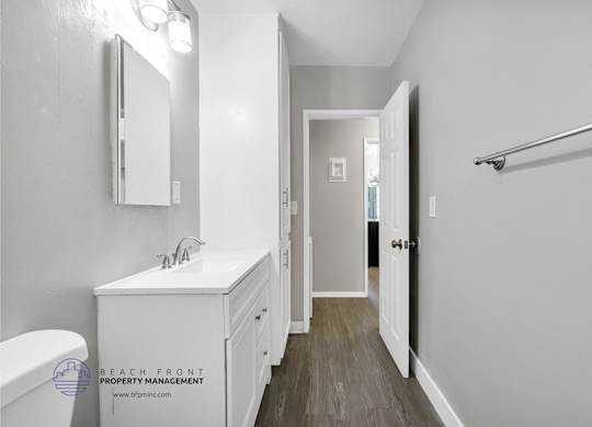 A white bathroom with a toilet, sink, mirror, and a wooden floor.