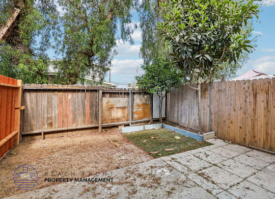 A backyard with a wooden fence and a tree.