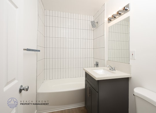 A white tiled bathroom with a sink, bathtub, and toilet.
