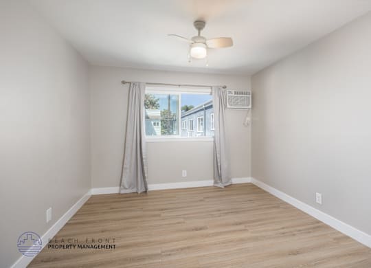 A room with a ceiling fan and a window with curtains.