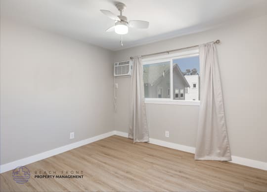 A room with a ceiling fan and a window with curtains.