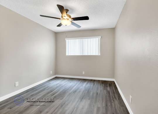 A room with a ceiling fan and a window with blinds.