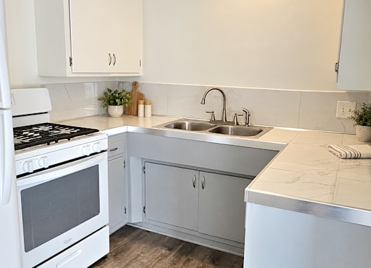 A white kitchen with a stove, sink, and cabinets.