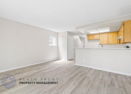 A spacious room with wooden flooring and a logo for Beach Front Property Management.