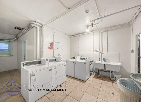 A clean, empty room with a washing machine and a dryer, with the logo of Beach Front Property Management in the corner.