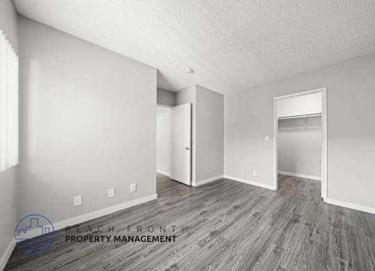 A room with wooden flooring and white walls, with a logo for Beach Front Property Management in the bottom left corner.