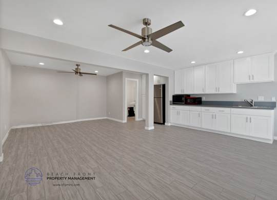 A spacious kitchen and living room with a ceiling fan and lighting fixtures.