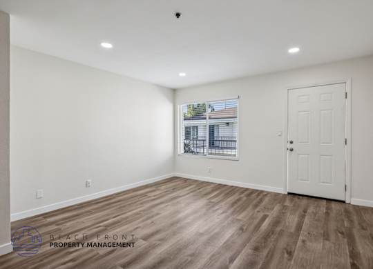 A spacious room with wooden flooring and a view of a building through the window.