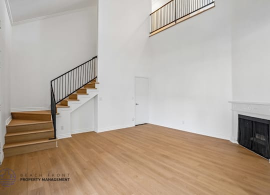 A spacious room with a fireplace and a staircase with a black railing.