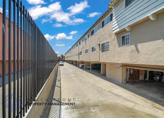 A view of a street with buildings on both sides and a fence on the left.