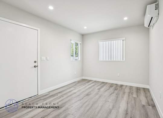 A room with a white door, window with blinds, and a wooden floor.