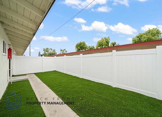 A white fence with a green lawn in front of a building.