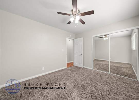 A spacious room with a ceiling fan and a sliding glass door leading to a balcony.