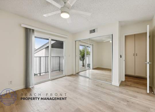 A spacious room with a sliding glass door leading to a balcony, a ceiling fan, and a logo for Beach Front Property Management.