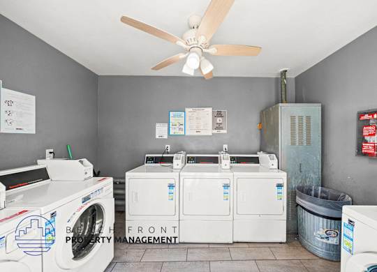 A laundry room with a washer and dryer, a fan, and a trash can.