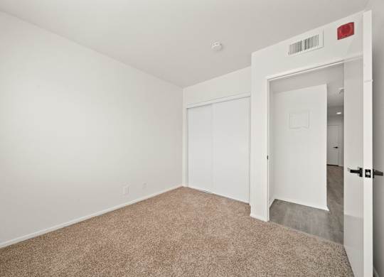 a bedroom with white walls and carpet and a door to a closet