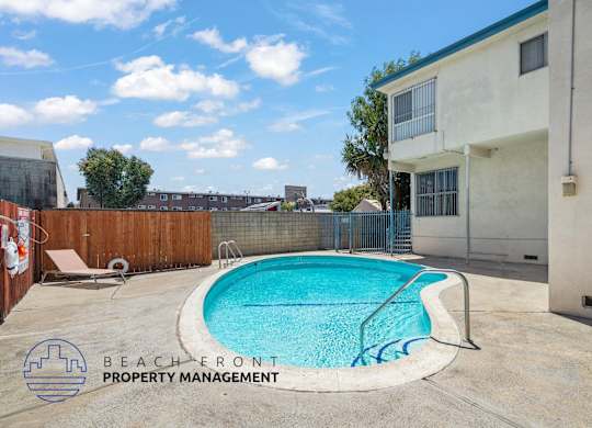 A pool in a backyard with a fence and a building in the background.