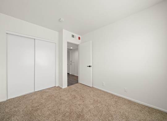 a bedroom with white walls and carpet and a door to a hallway