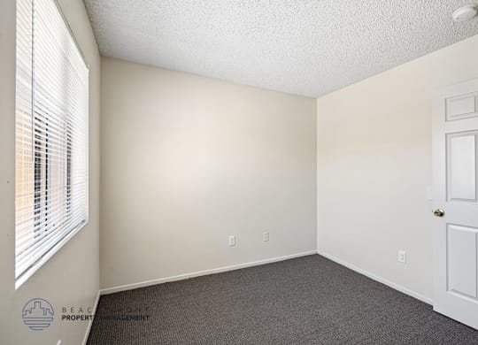 A room with a white door, carpeted floor, and a window with blinds.