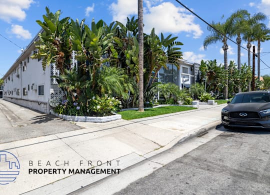 a car is parked on the street in front of a white building with palm trees