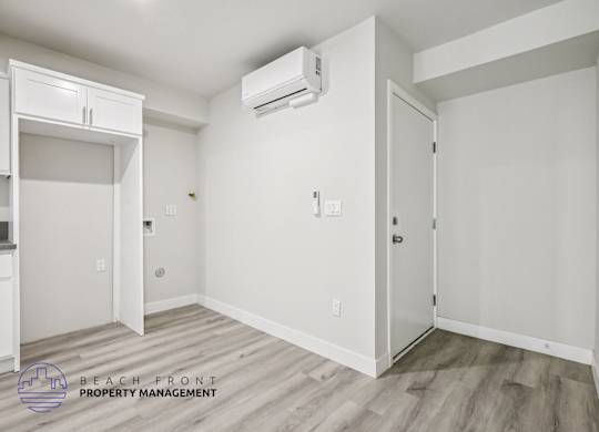 A white room with a wooden floor and a wall-mounted air conditioner unit.