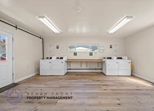A room with a wooden floor and white walls has a row of printers on a table.