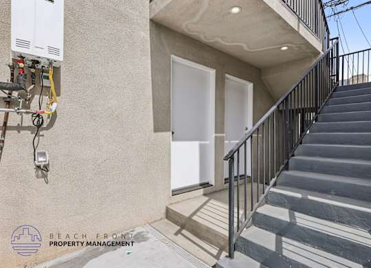 A staircase with a metal railing leads to a white door on a tan building.