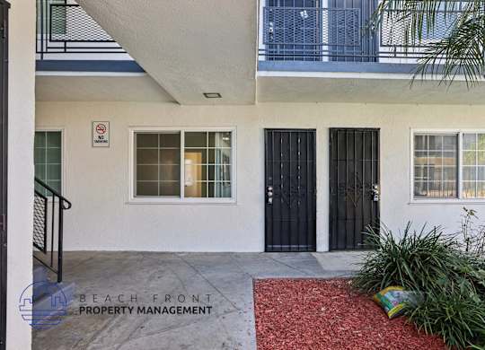 A white building with a black door and a no parking sign on the wall.