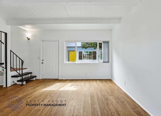 A spacious room with wooden floors and white walls, featuring a staircase with black railings.