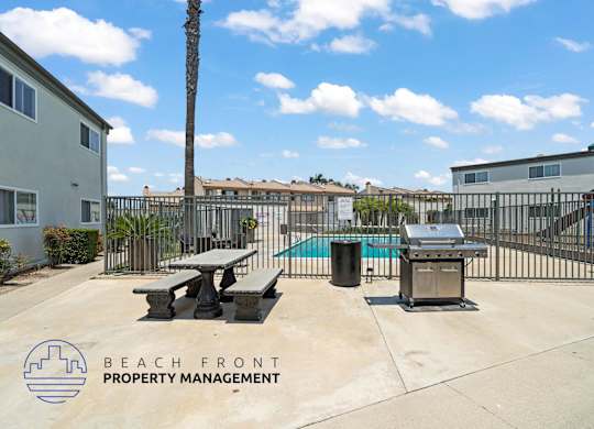 A pool area with picnic tables and a grill is managed by Beach Front Property Management.