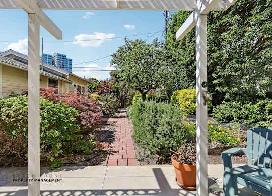 A white pergola is over a patio with a blue chair.