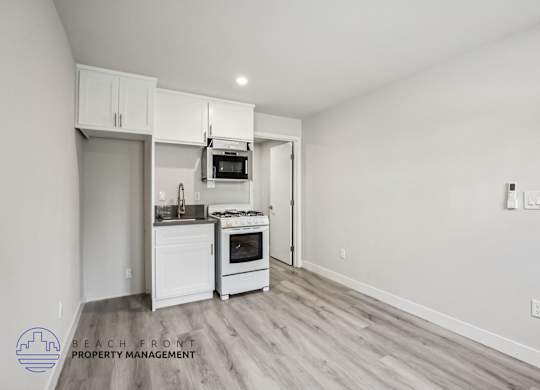 A kitchen with white cabinets and appliances in a room with wooden flooring.