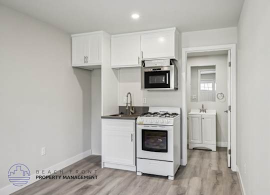 A kitchen with white cabinets and appliances, a microwave above the stove, and a doorway leading to another room.
