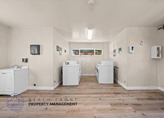 A laundry room with two washing machines and a dryer, and a sign that says Beach Front Property Management.