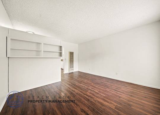 A room with wooden floors and white walls, with a shelving unit and a door.