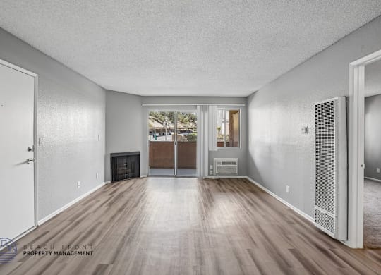 A spacious room with wooden floors and white walls, featuring a fireplace and sliding glass doors.