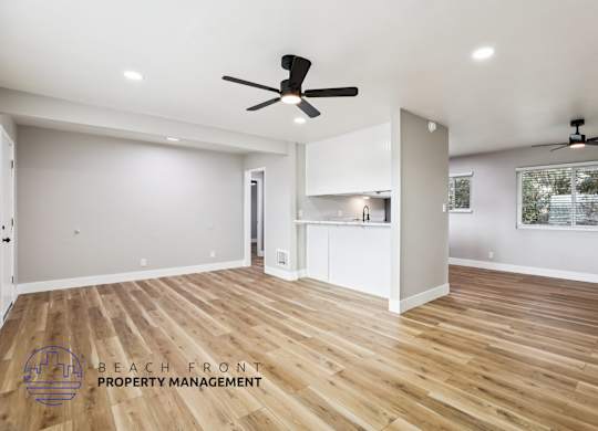 A spacious room with wooden floors and two ceiling fans.