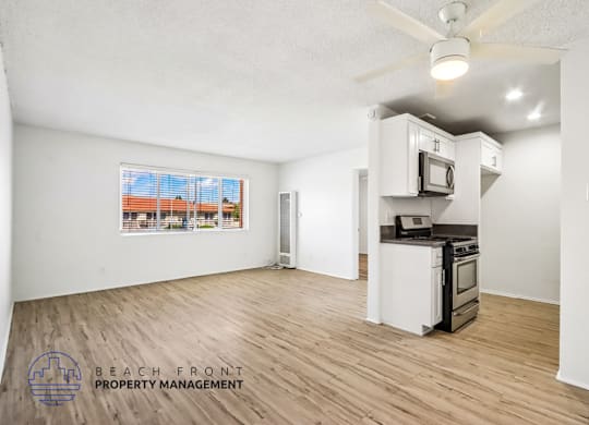 A spacious room with a kitchenette and a window overlooking a beach.