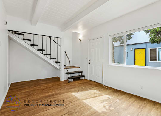 A spacious room with a staircase and a window overlooking a blue building.