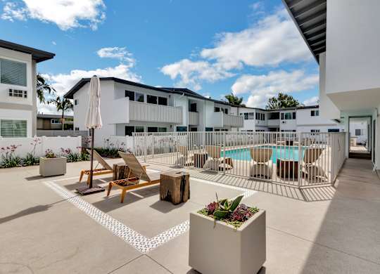 A sunny day at a poolside with chairs and a table.