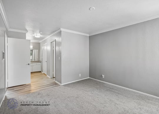 A spacious room with a carpeted floor and white walls, with a doorway leading to another room.