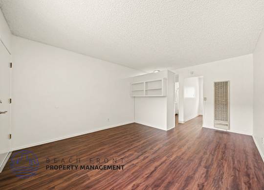 A room with wooden floors and white walls, with a logo for Beach Front Property Management in the bottom left corner.