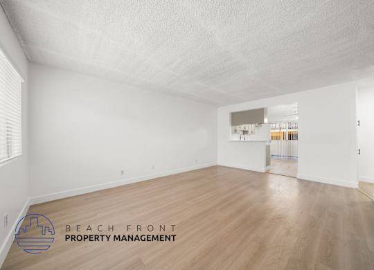 A spacious room with wooden flooring and white walls, with a logo for Beach Front Property Management in the bottom left corner.