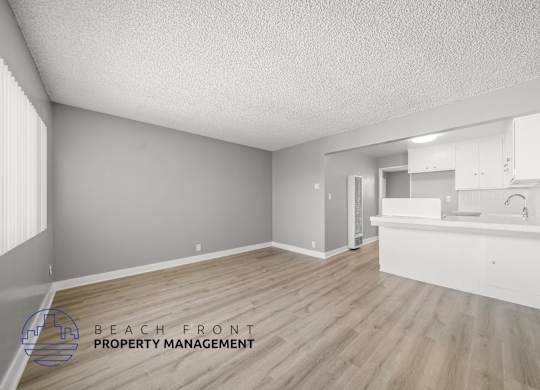 A spacious room with wooden flooring and a kitchen area with white cabinets.