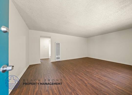 A room with wooden floors and white walls, with a door in the background.